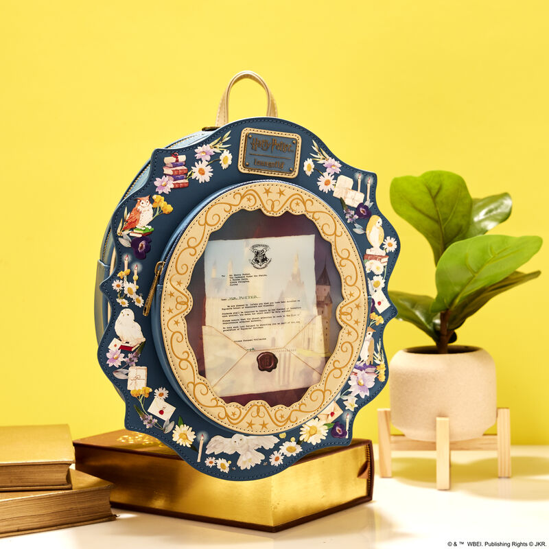 Loungefly Harry Potter Hogwarts Castle Cameo Mini Backpack sitting on a book with gold edges, next to a plant against a yellow-gold background